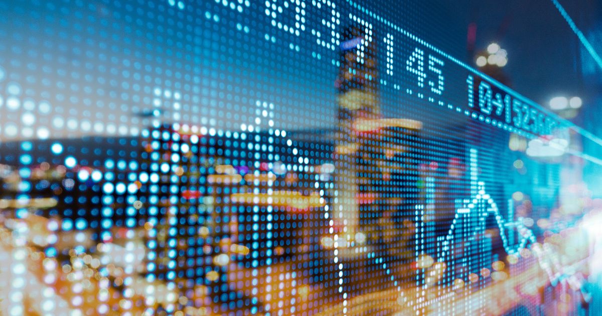 Nighttime city skyline with a blue dotted data overlay and a fluctuating stock chart in the foreground, suggesting financial data visualization.