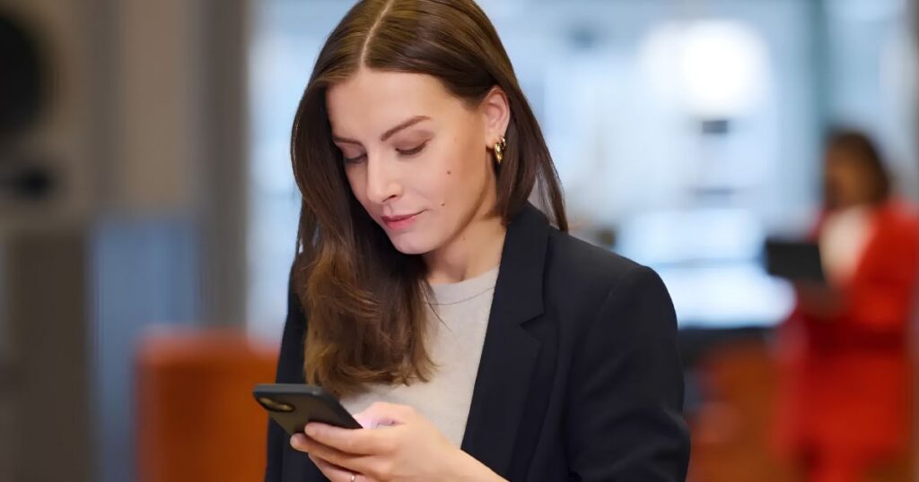 Businesswoman in a navy blazer looking at her smartphone in a modern office setting.