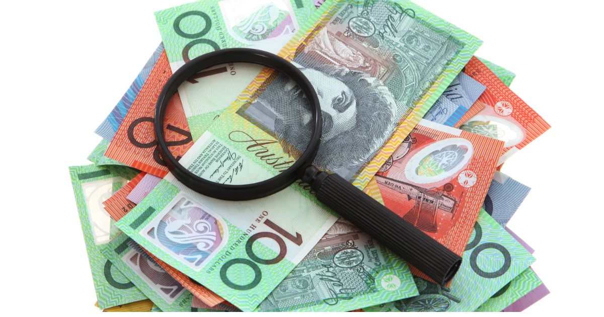 Magnifying glass placed over a pile of colorful banknotes, suggesting money inspection or investigation of cash